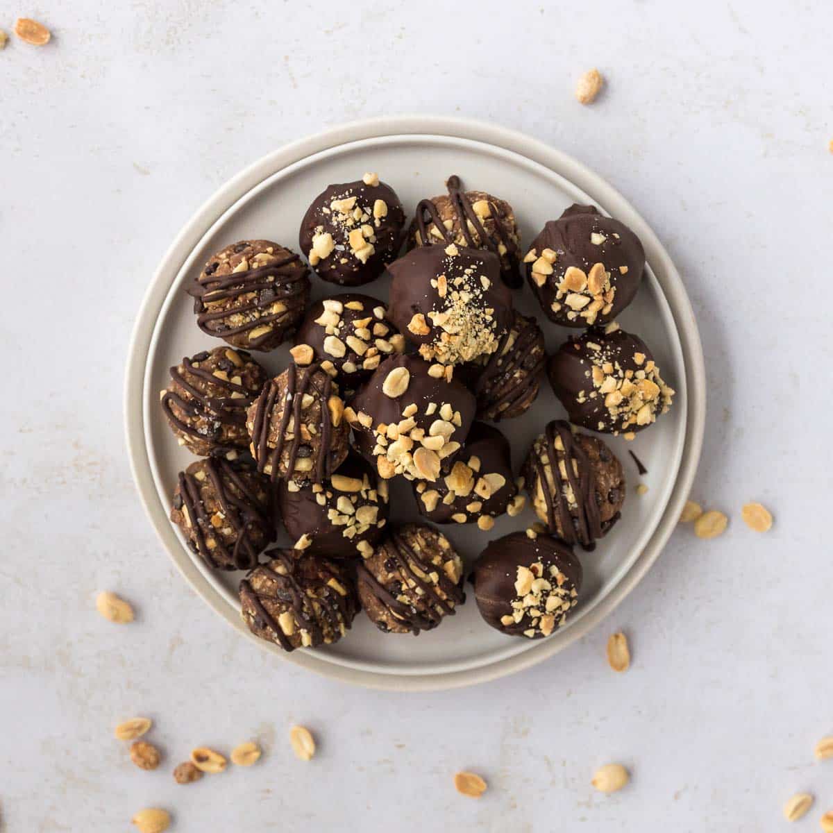 Snickers protein balls on a white plate, made with dates, peanut butter, chocolate, and topped with chopped peanuts