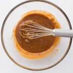 Tahini, almond butter, maple syrup, egg, and vanilla being whisked together for chocolate chip protein cookies