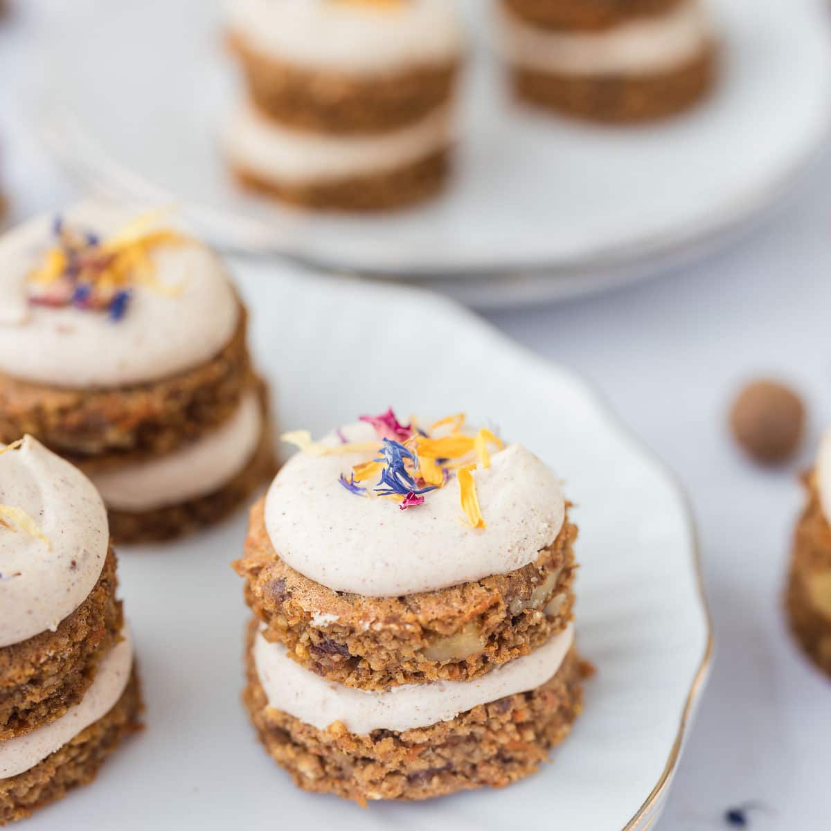 mini carrot cakes with cream cheese frosting and edible flowers on white scalloped plates