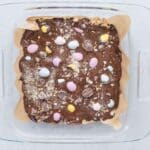 Melted chocolate poured over cookie dough layer with crushed mini eggs on top