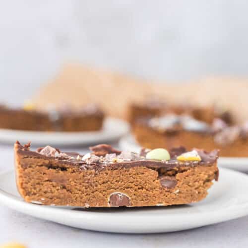 Cloes up of Mini egg cookie dough protein bar topped with chocolate and crushed Cadbury mini eggs on white plate