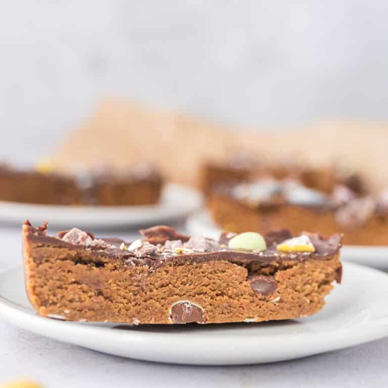 Cloes up of Mini egg cookie dough protein bar topped with chocolate and crushed Cadbury mini eggs on white plate