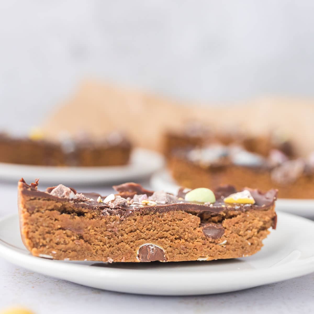 Cloes up of Mini egg cookie dough protein bar topped with chocolate and crushed Cadbury mini eggs on white plate