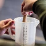 Close-up of hands stirring water and gelatin in measuring cup