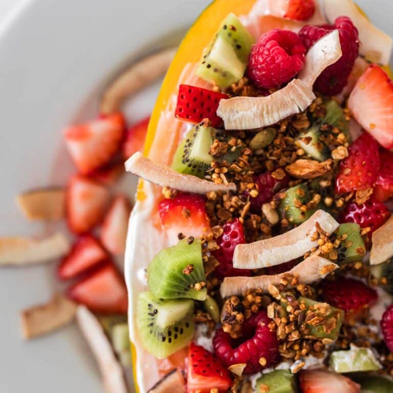 closeup of papaya breakfast bowl topped with berries, kiwis, coconut, granola