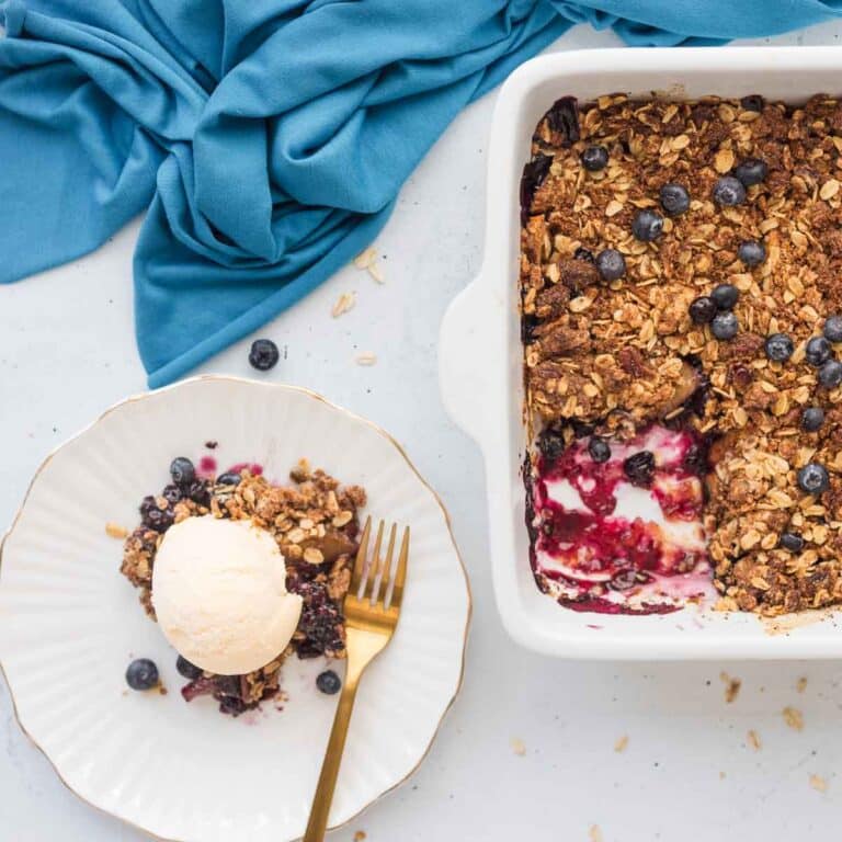 Peach Blueberry Cobbler slice on plate topped with ice cream with pan of remaining cobbler beside