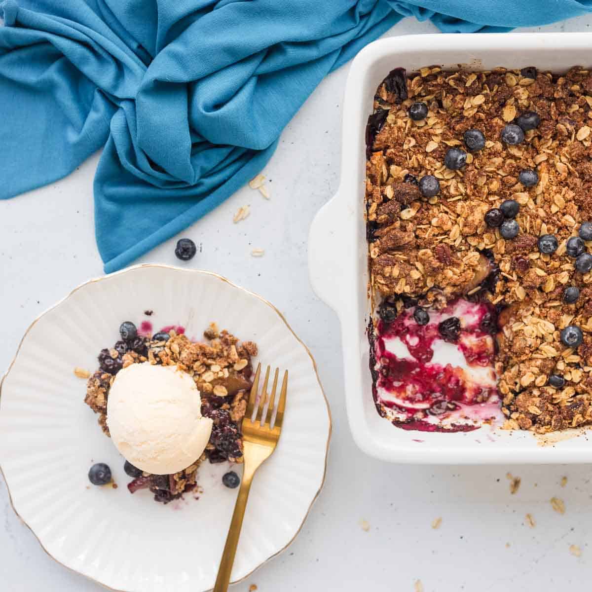 Peach Blueberry Cobbler slice on plate topped with ice cream with pan of remaining cobbler beside