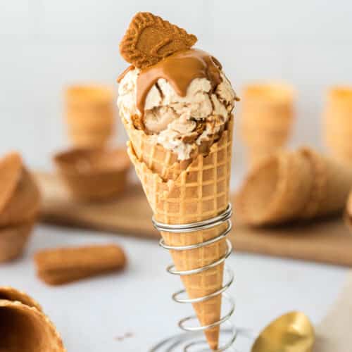 Scoops of high protein Biscoff ice cream in a waffle cone topped with melted Biscoff spread and Lotus Biscoff cookies.