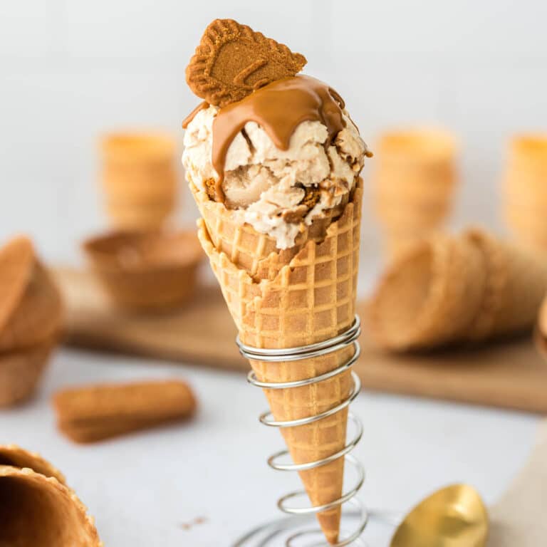 Scoops of high protein Biscoff ice cream in a waffle cone topped with melted Biscoff spread and Lotus Biscoff cookies.