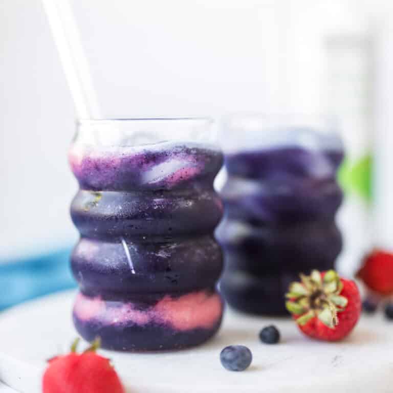 Healthy strawberry blueberry electrolyte mocktail made with coconut water, fresh strawberries, blueberries, and ice in a clear glass.