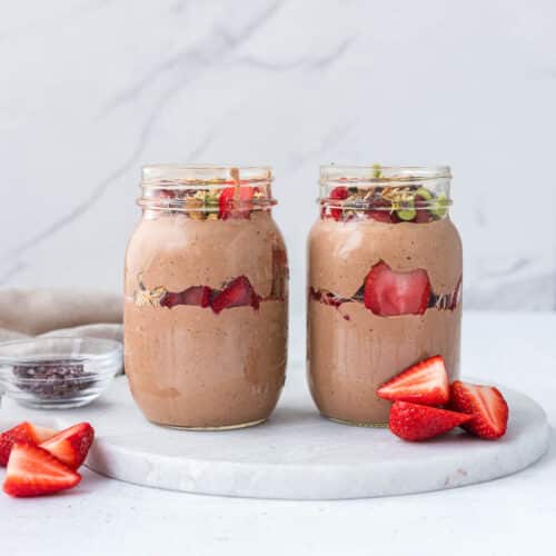 High protein Dubai chocolate overnight oats layered with creamy chocolate blended oats, pistachio cream, toasted kataifi, strawberries, and cacao nibs in glass mason jars