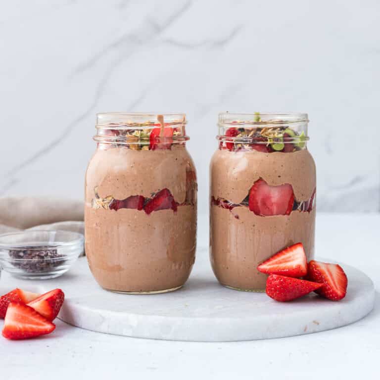 High protein Dubai chocolate overnight oats layered with creamy chocolate blended oats, pistachio cream, toasted kataifi, strawberries, and cacao nibs in glass mason jars
