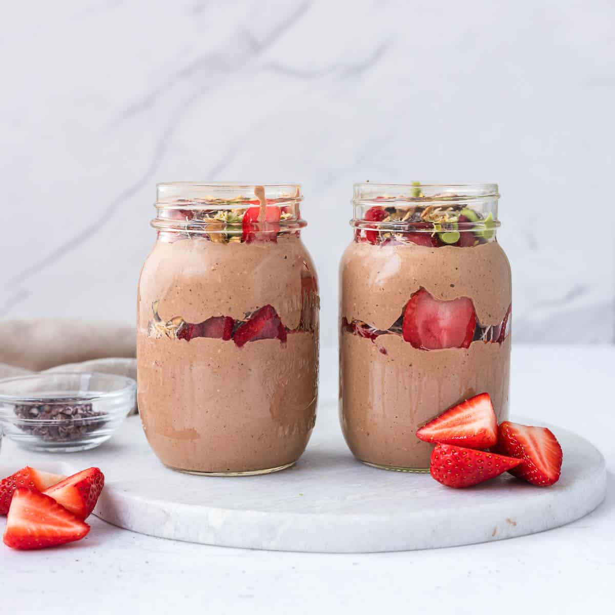 High protein Dubai chocolate overnight oats layered with creamy chocolate blended oats, pistachio cream, toasted kataifi, strawberries, and cacao nibs in glass mason jars