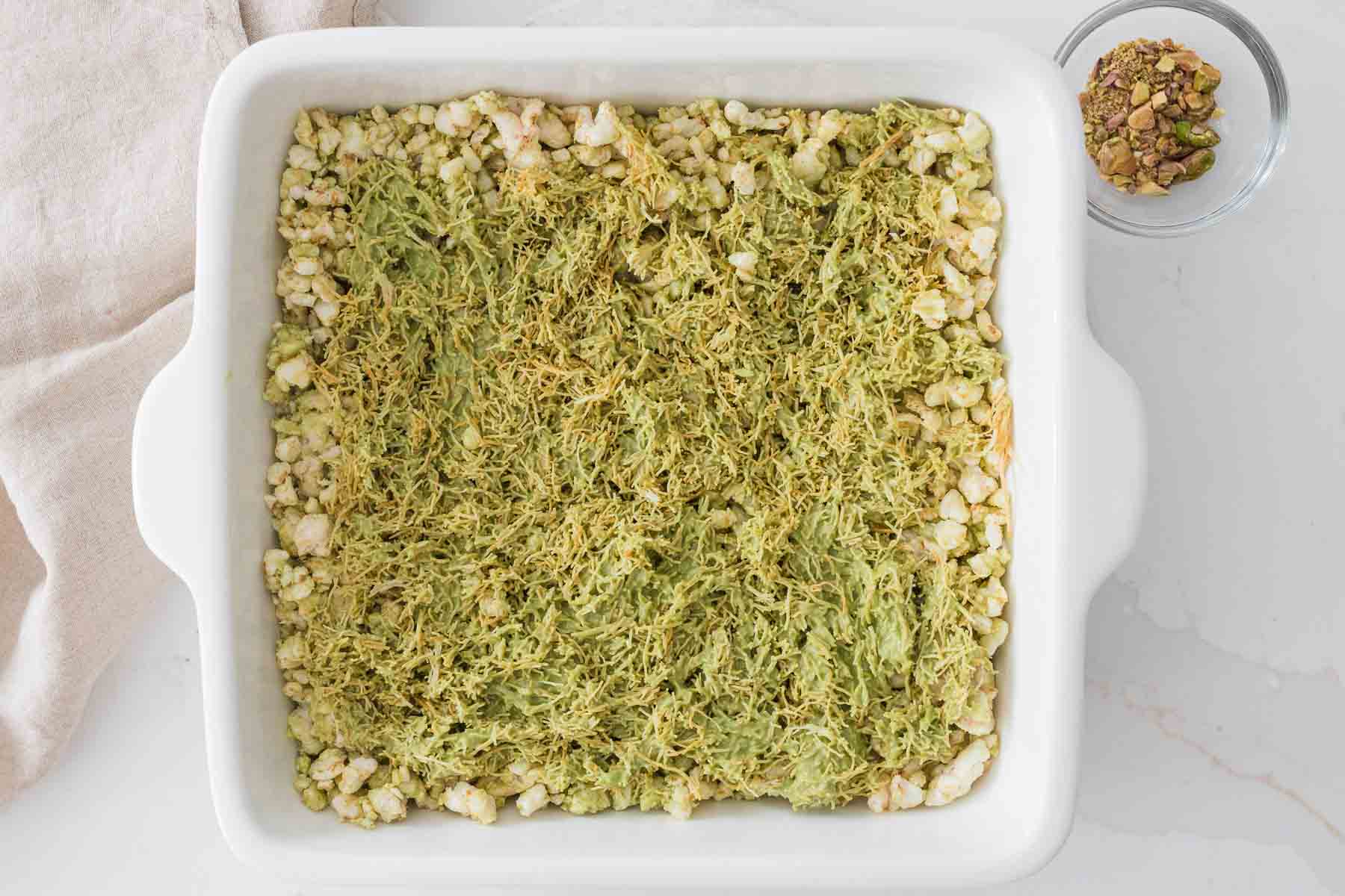 Spread the pistachio kataifi layer over the rice cake base.