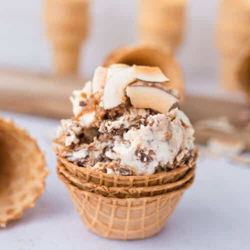 High-protein Samoa cottage cheese ice cream in a waffle bowl cone topped with toasted coconut, date caramel, and chocolate drizzle