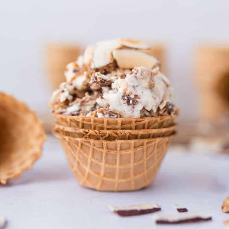 High-protein Samoa cottage cheese ice cream in a waffle bowl cone topped with toasted coconut, date caramel, and chocolate drizzle