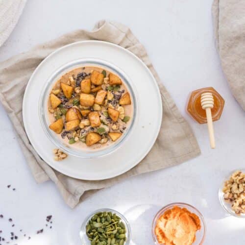 Blended pumpkin cheesecake overnight oats topped with cooked apple pieces, pumpkin seeds, walnuts, cacao nibs, honey and cinnamon.